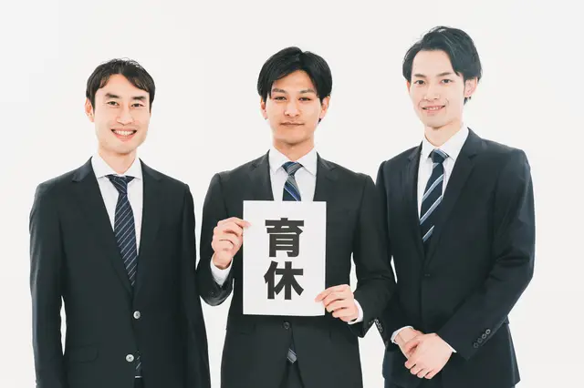 育休と書かれた紙をもつ3人の男性ビジネスパーソン